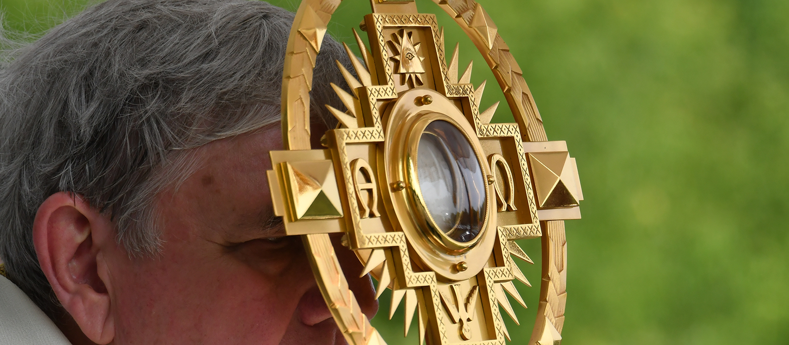 Archbishop holding monstrance with Eucharist to forehead.