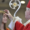 Bishop with crozier anointing woman's forehead.