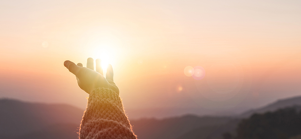 Arm outstretched to sunset in a helping, hopeful gesture.